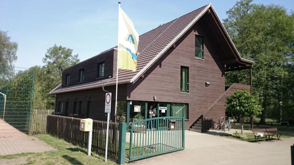 Dunkles Holzhaus der Jugendherberge Lübben mit Fahnenmast und Eingang zur Rezeption